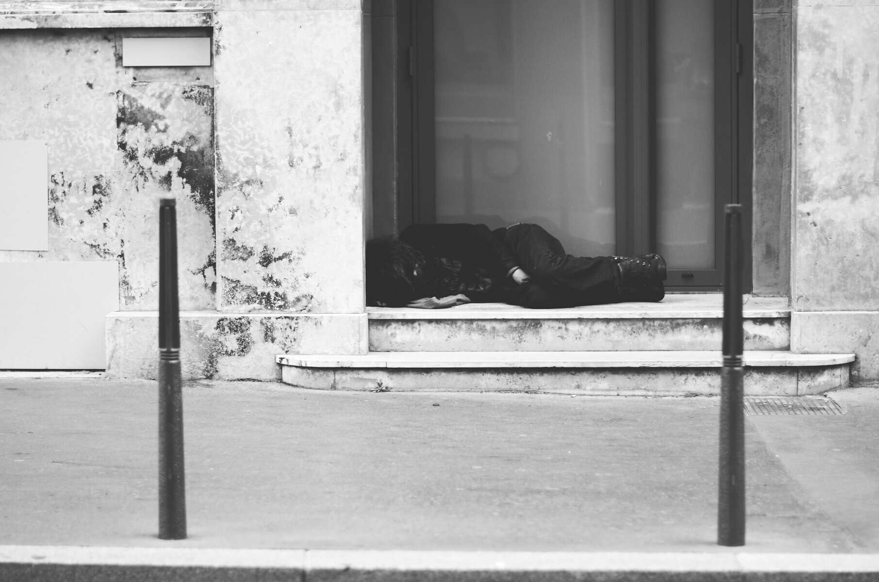 A person sleeping rough in a window sill of a building.