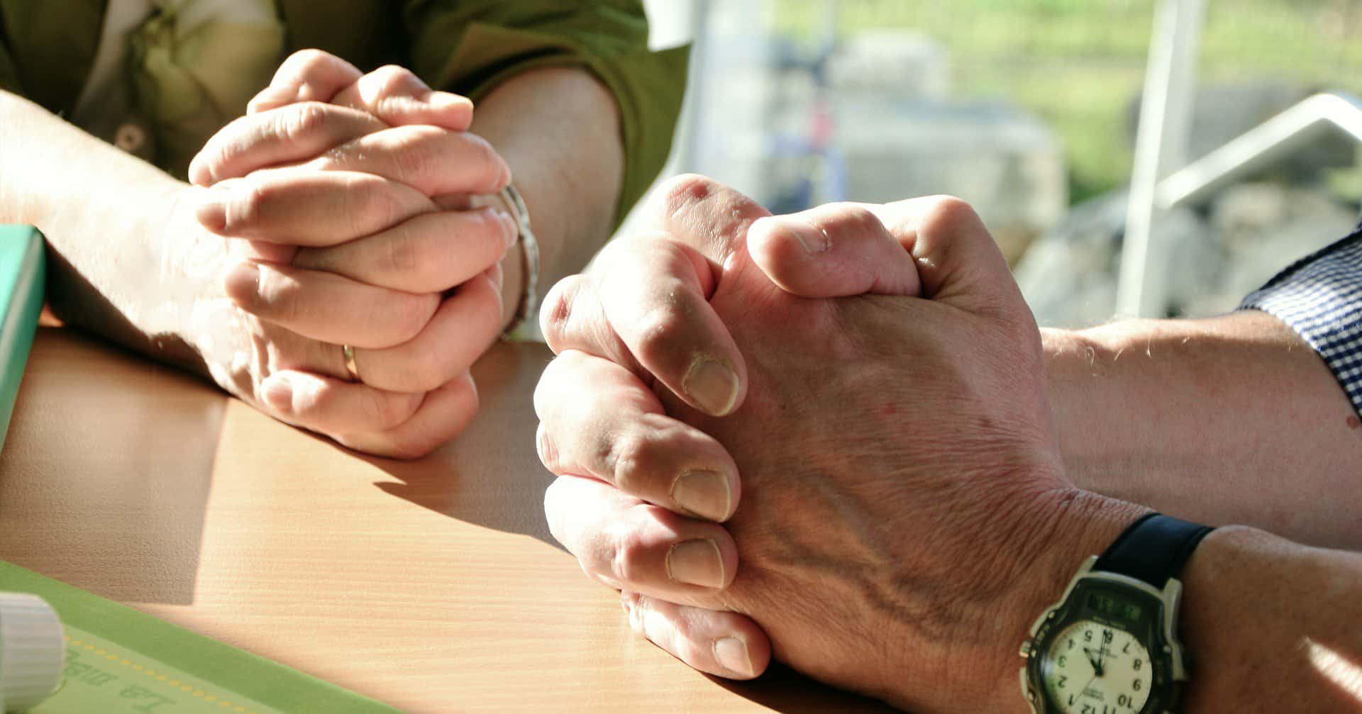 The hands of two people folded in prayer are shown.