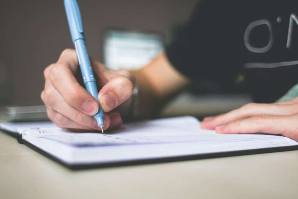 A person is shown from the shoulder down holding a pen over blank paper.
